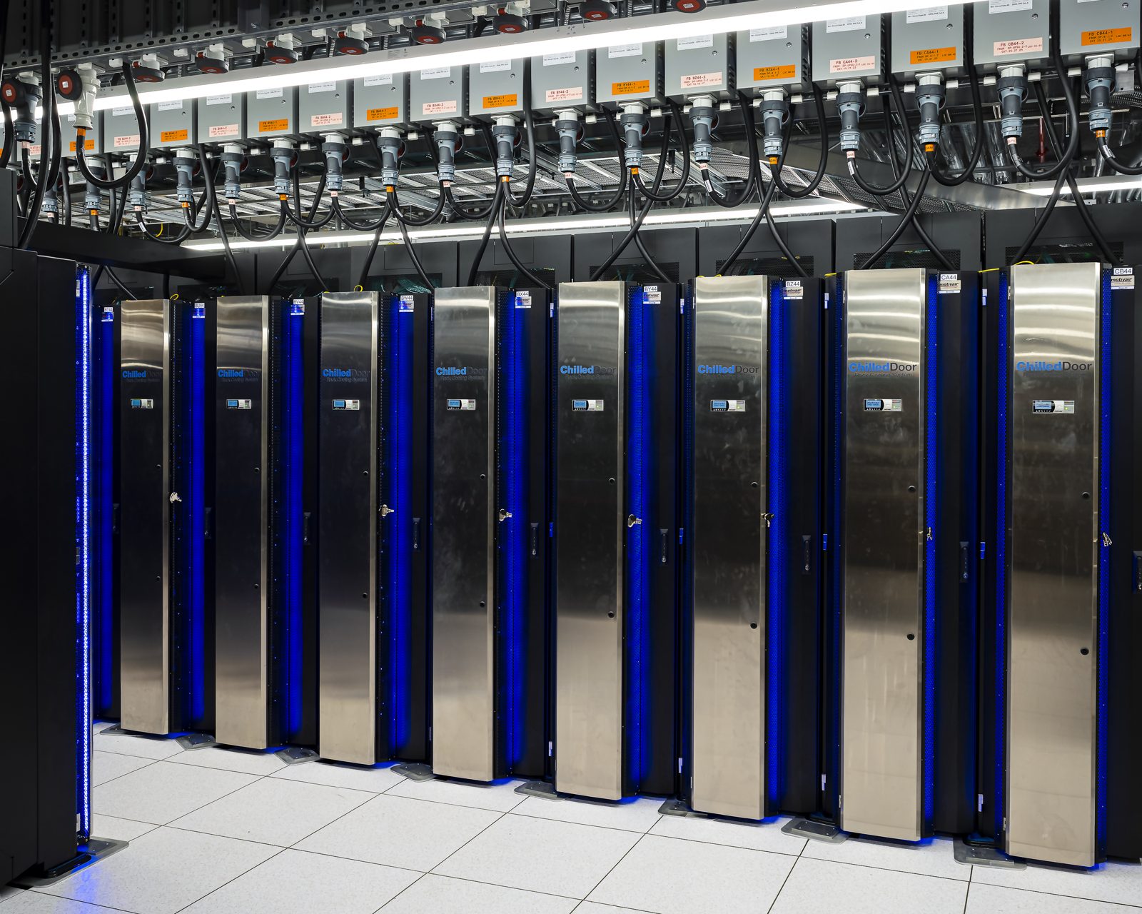 A row of HPE Cray EX cabinets at Oak Ridge with coolant piping and cabling running overhead