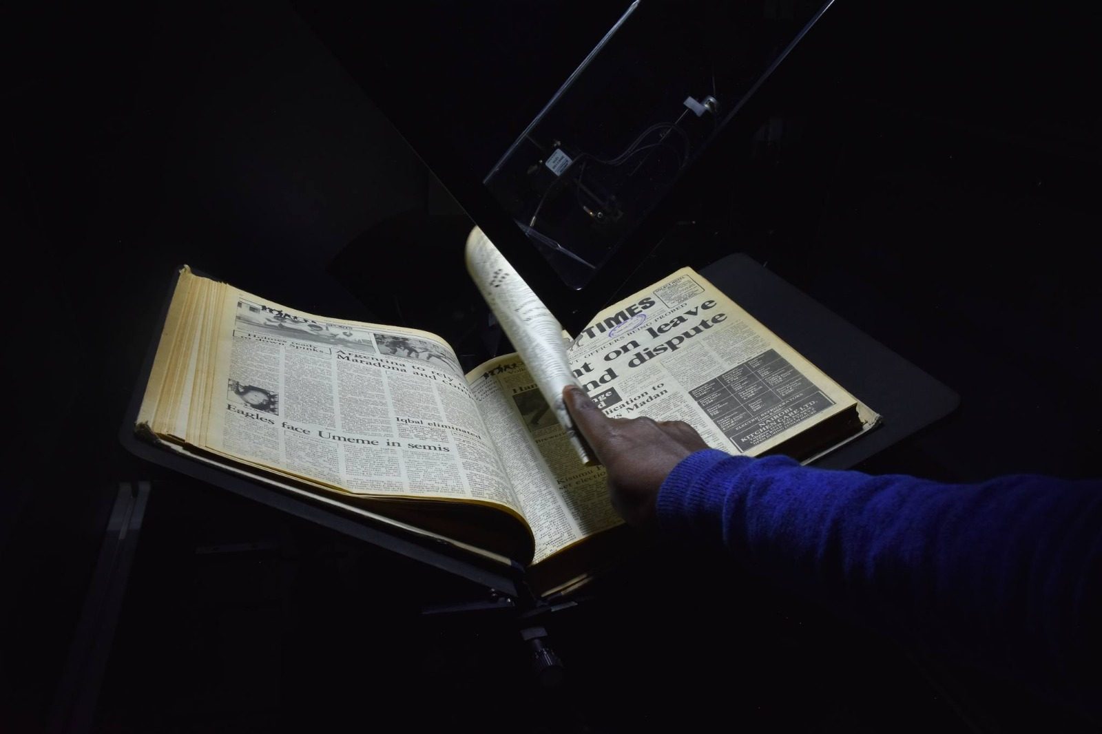 A bound newspaper volume on a Qidenus book scanner, lit for high-resolution capture